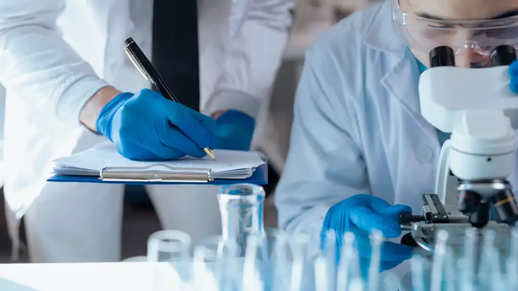 Lab techs using a microscope and a pen and paper to record findings