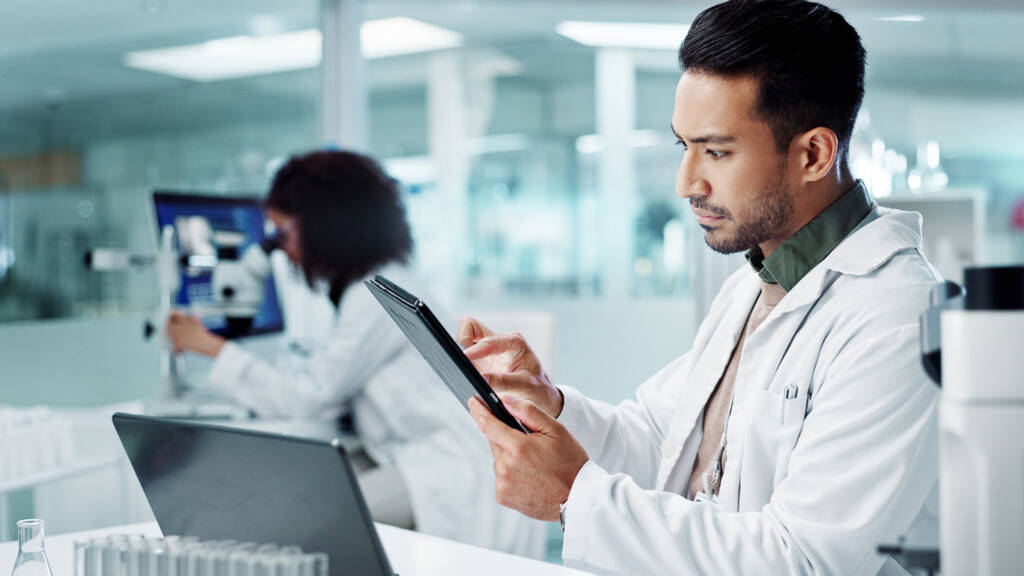 Technicians working in a laboratory. The technician in the front is analyzing data in the LIMS on his tablet - Best LIMS of 2025