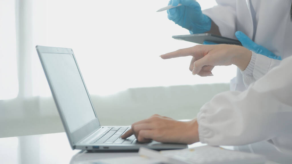 Lab professional typing on a laptop while a colleague points at the screen, representing LIMS integration and automated data management in a laboratory