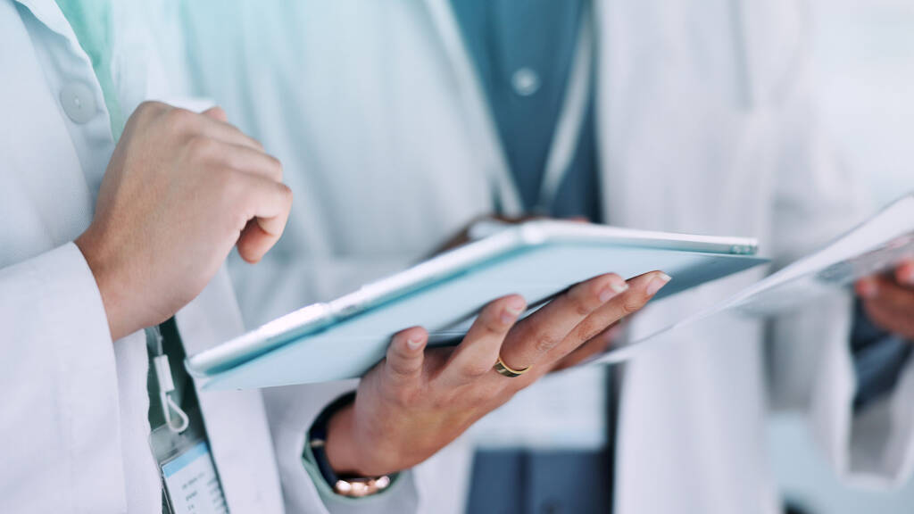 Close-up of a lab professional in a white coat reviewing LIMs data on a tablet.