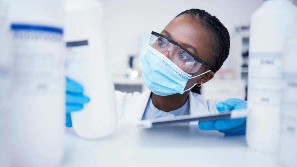 Laboratory technician inspecting chemical containers while managing reagents and supplies tracked through a LIMS inventory module.